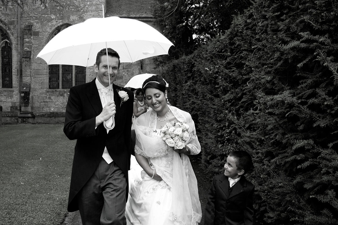 Bride and groom walking under a white umbrella at Wroxall Abbey Estate